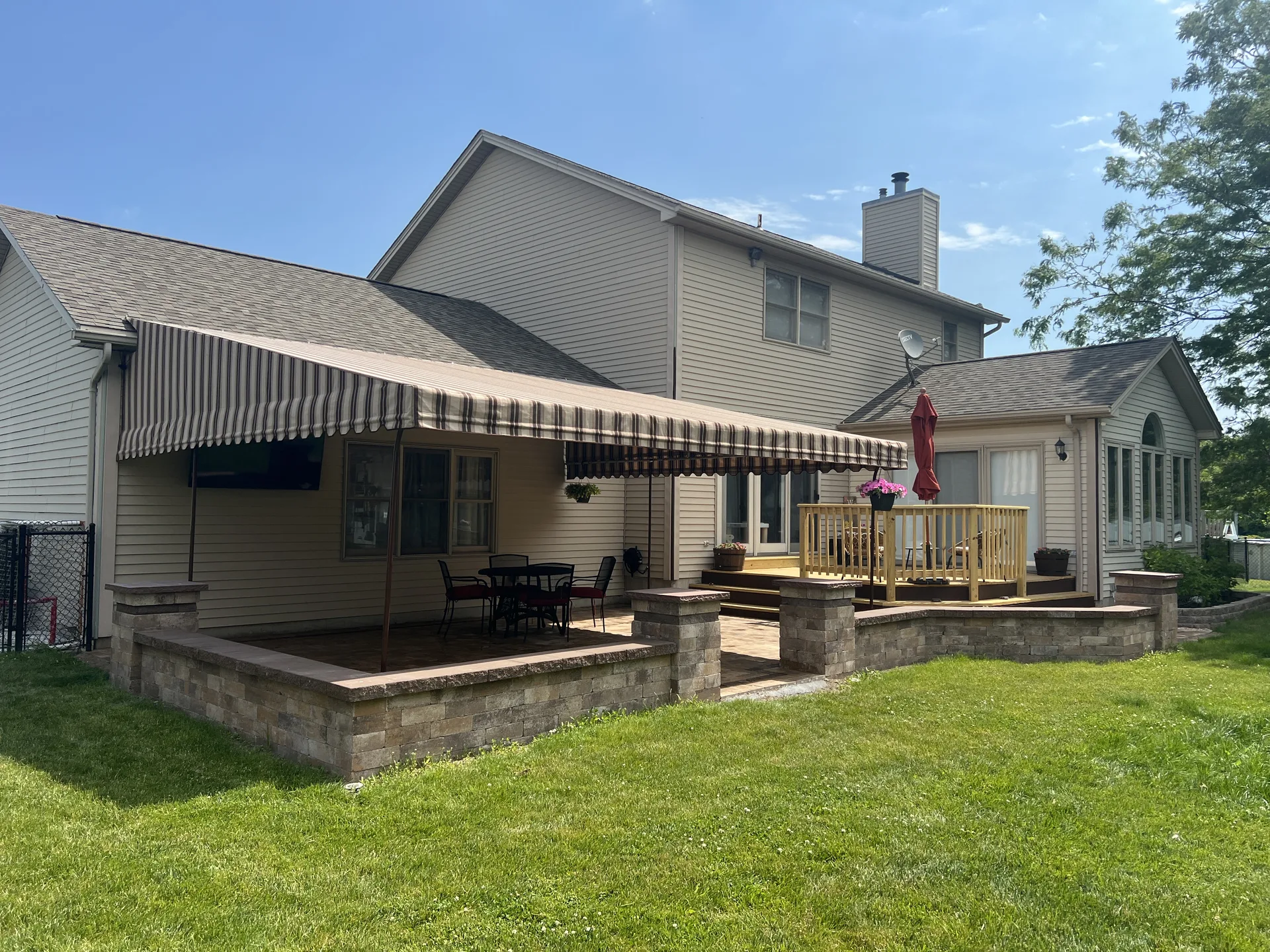 Raised paver patio with stone columns and a striped awning beside a home